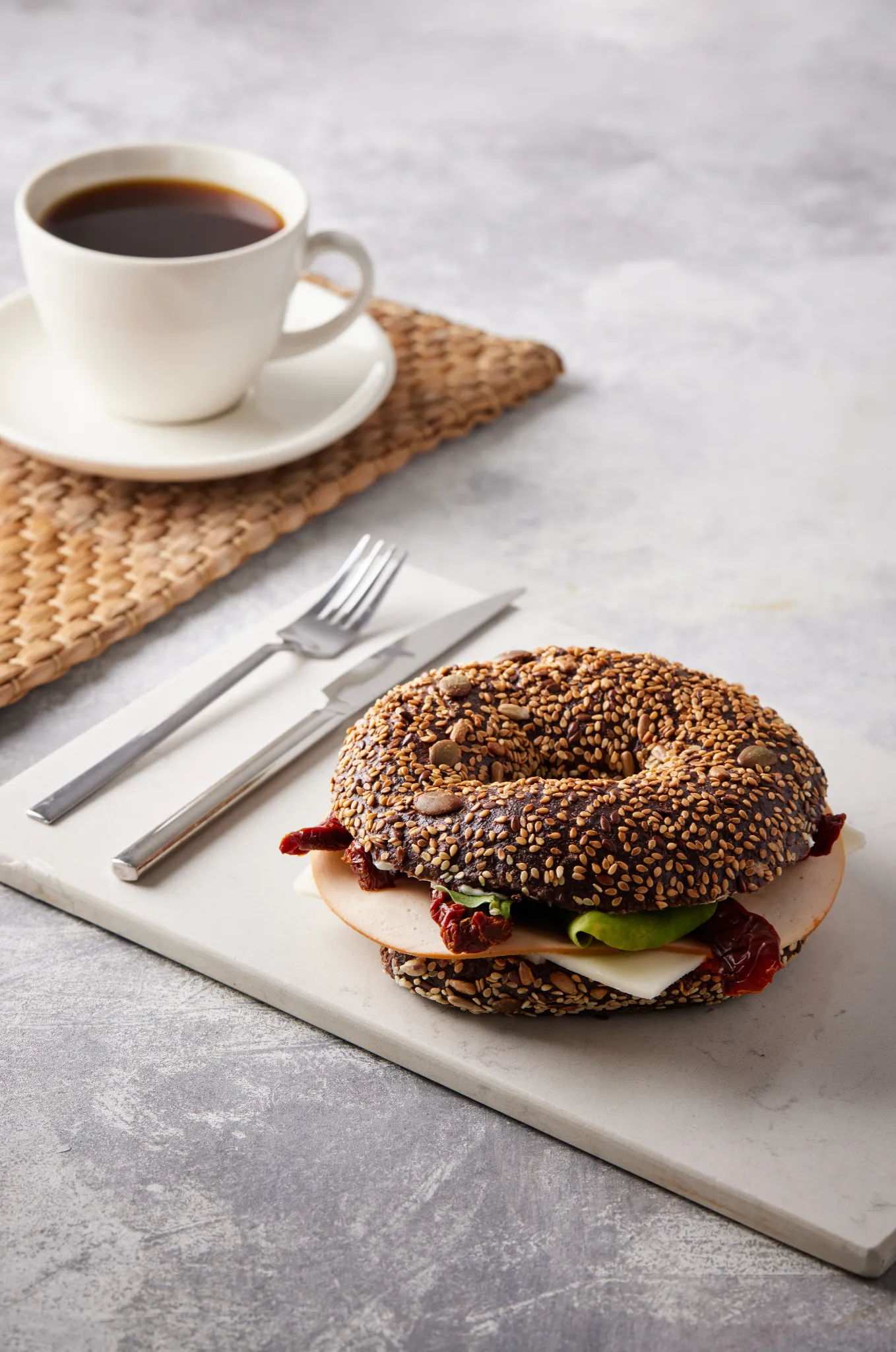 Atlanta food styling — seeded bagel sandwich with black coffee on stone surface