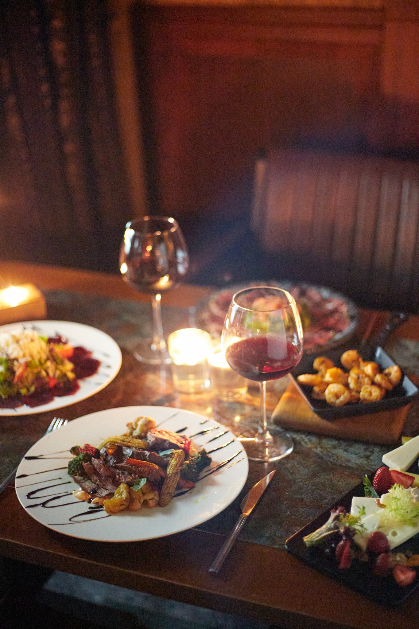 Candlelit dinner table with red wine, steak and seafood plates – Roswell restaurant photographer.