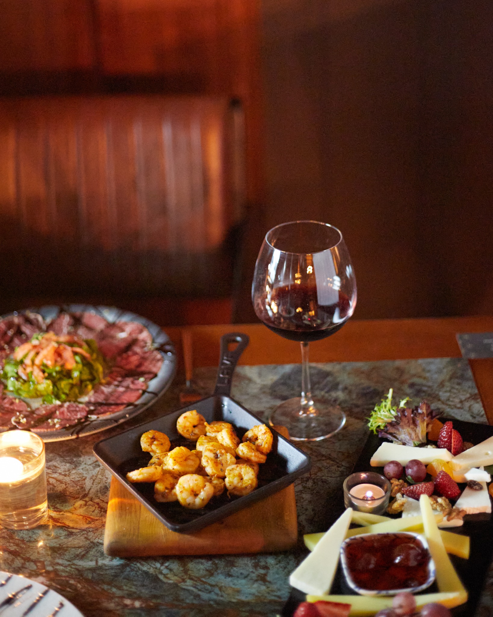 Sautéed shrimp in cast-iron pan with red wine in moody restaurant light – on-location food photography.